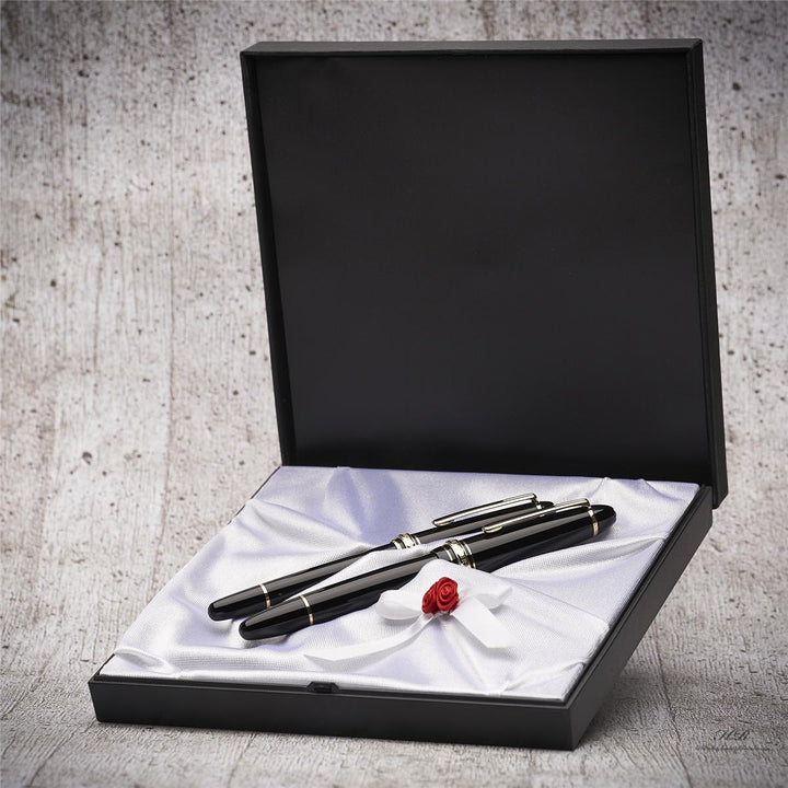 Zwei schwarze Füller liegen in edler Geschenkbox im Hochzeitsdesign vor Hintergrund in grauer Holzoptik