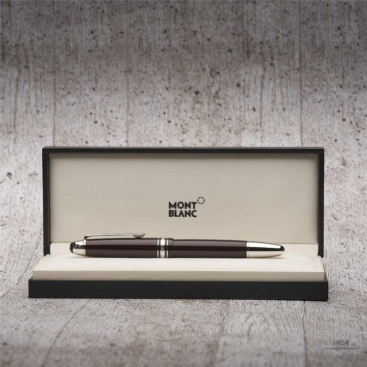 Dunkelbrauner Rollerball mit silbernen Beschlägen in offener Originalbox vor grauem Holzoptik-Hintergrund