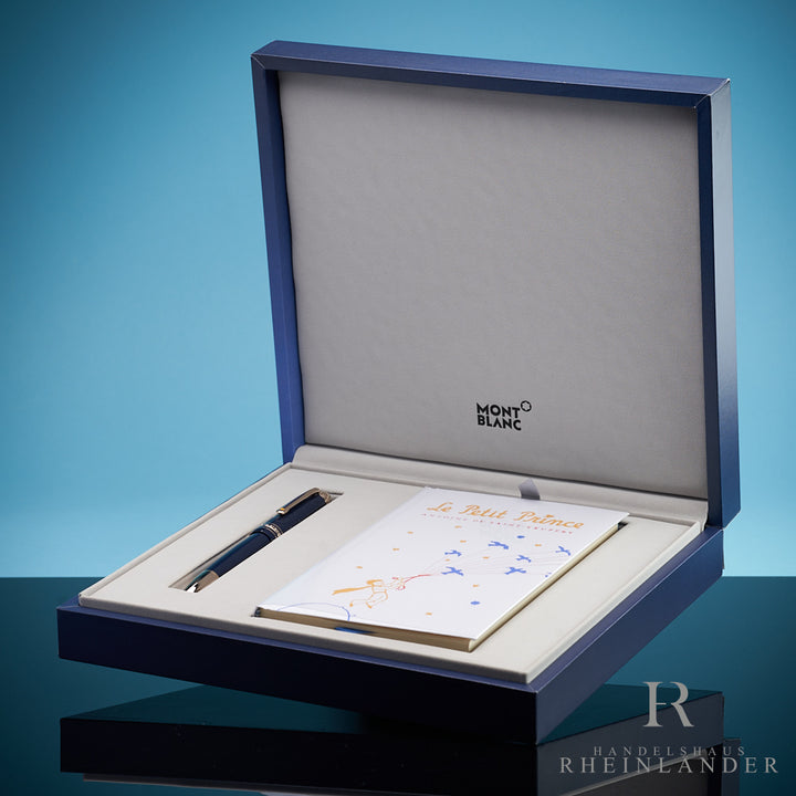Blauer Füller neben Le petit Prince Buch in Montblanc Geschenkschatulle liegend vor blauem Hintergrund