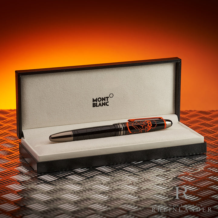 Schwarzer Füller mit orange gravierter Kappe in Originalbox auf Riffelblech vor orangem Hintergrund