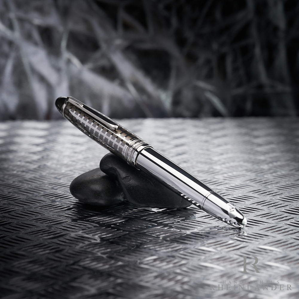 Silberner Füller mit gemusterter Kappe lehnt auf dunkelgrauen Steinen die auf Riffelblech liegen