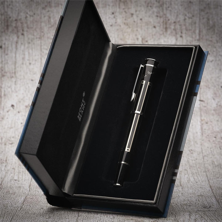 Silber-schwarzer Rollerball liegt in offener, halb aufgestellter Buchbox vor hellgrauem Holzoptik-Hintergrund