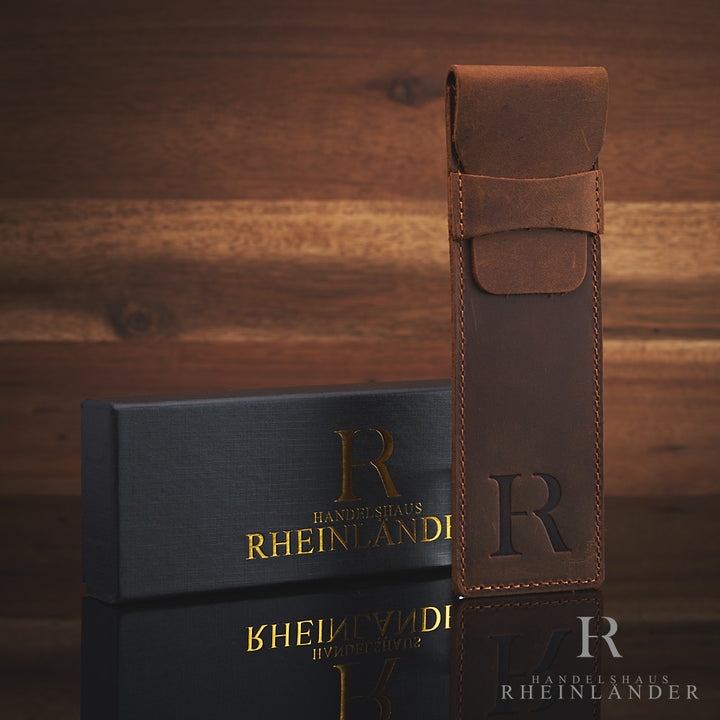 braunes Lederetui mit Logoprägung und Geschenkbox vor Holzwand