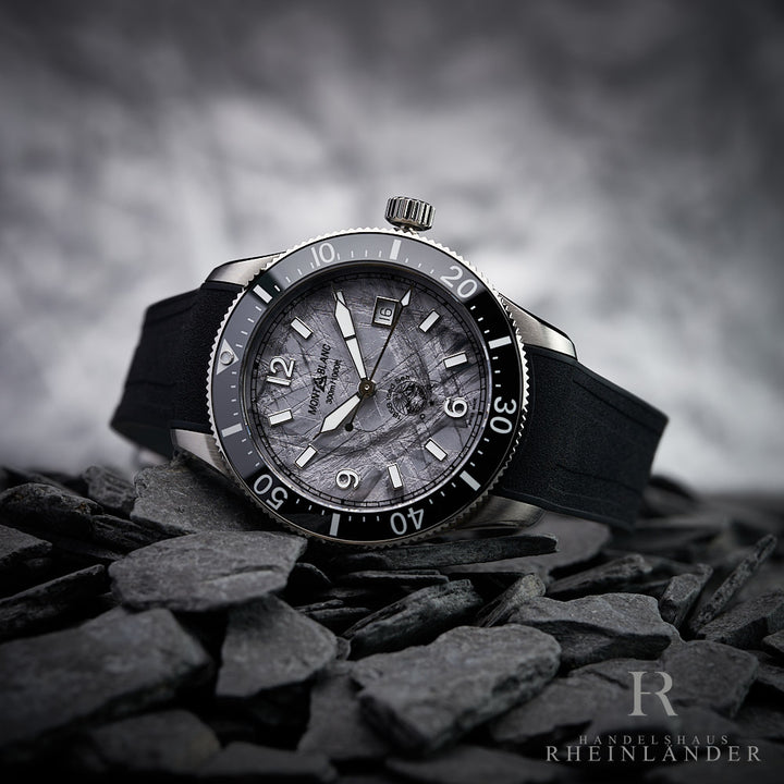 Graue Armbanduhr von Montblanc mit silbernen Details liegend auf dunkelgrauen Steinen fotografiert