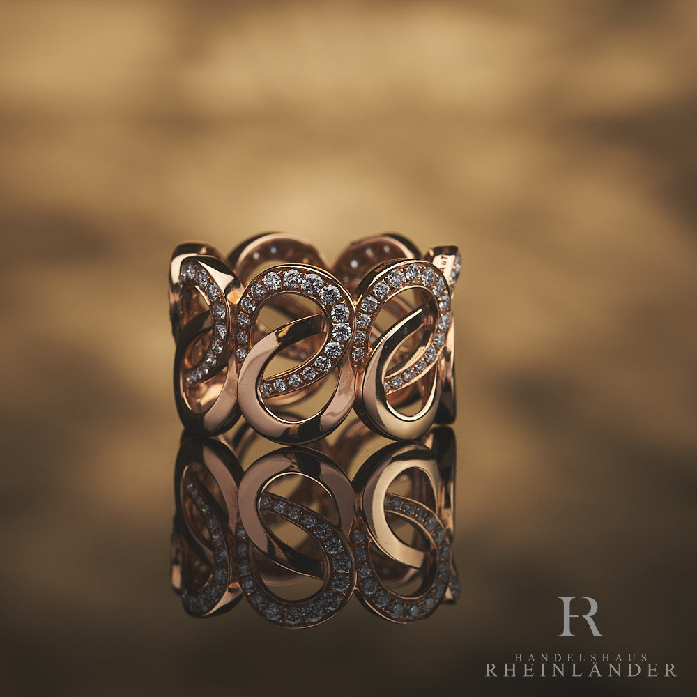 Roségoldener Ring mit geschwungener Schleifenstruktur und Diamantbesatz vor hellbraunem Hintergrund