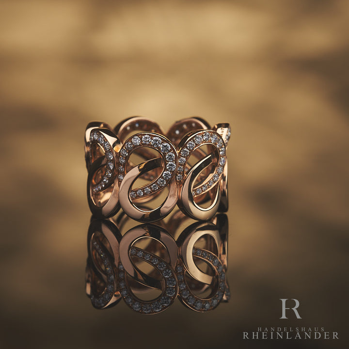 Roségoldener Ring mit geschwungener Schleifenstruktur und Diamantbesatz vor hellbraunem Hintergrund