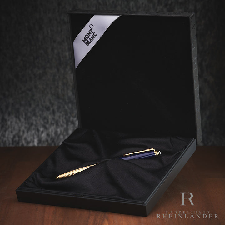 Goldener Kugelschreiber von Montblanc mit blauer Kappe in Solitairebox liegend, von oben auf Holztisch fotografiert