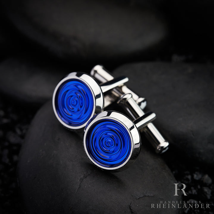 runde Manschettenknöpfe von Montblanc in silber mit blauem Inlay liegen auf schwazem Kies
