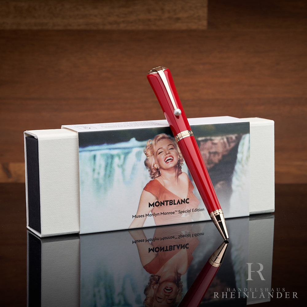 Roter Kugelschreiber lehnt an Monroe-Editionsbox vor braunem Holzhintergrund