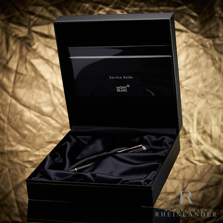Schwarzer Rollerball von Montblanc mit roségoldenen Beschlägen in Originalbox mit Service Guide vor goldenem Hintergrund fotografiert