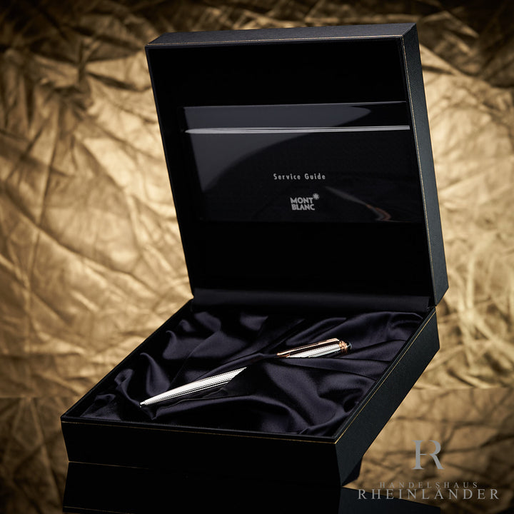 Silberner Kugelschreiber mit goldenen Details in schwarzer Montblanc-Box mit Serviceheft vor goldenem Hintergrund fotografiert