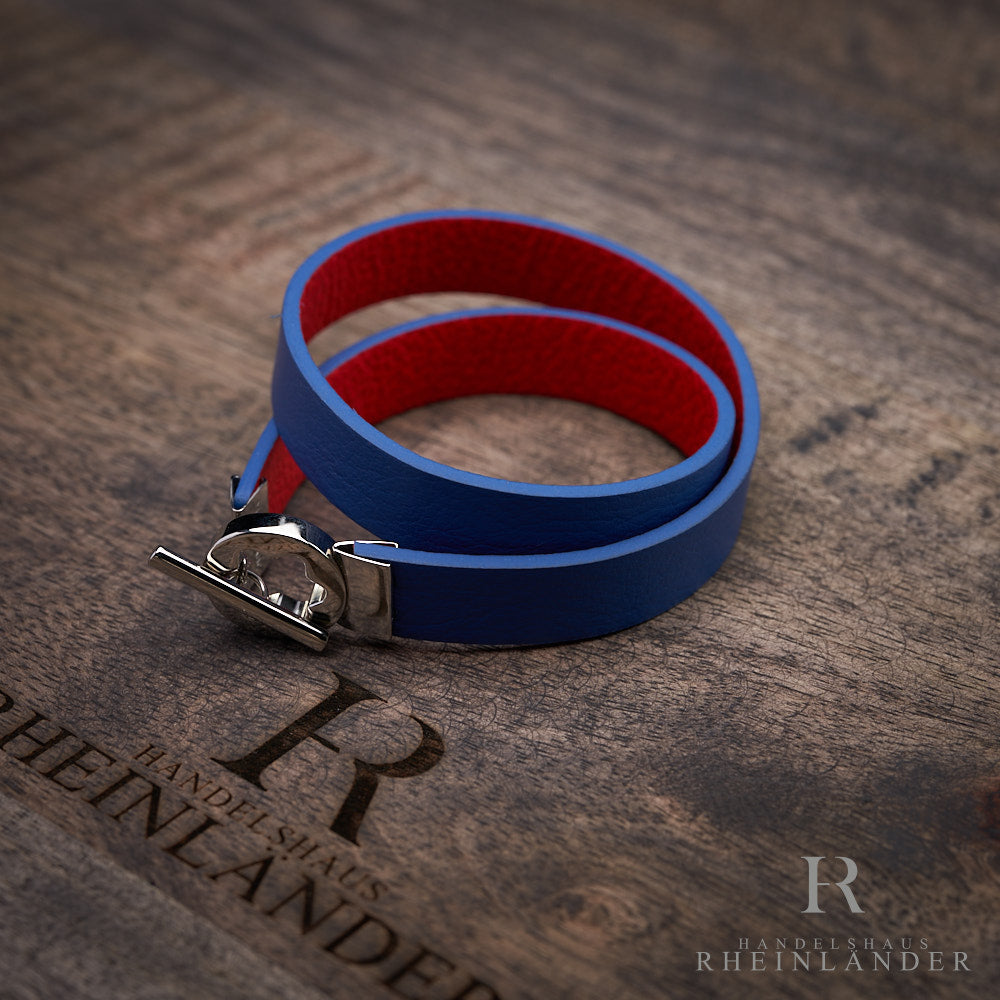 Blaues Armband, Innenseite rot, mit silbernem Knebelverschluss auf braunem Holz liegend fotografiert