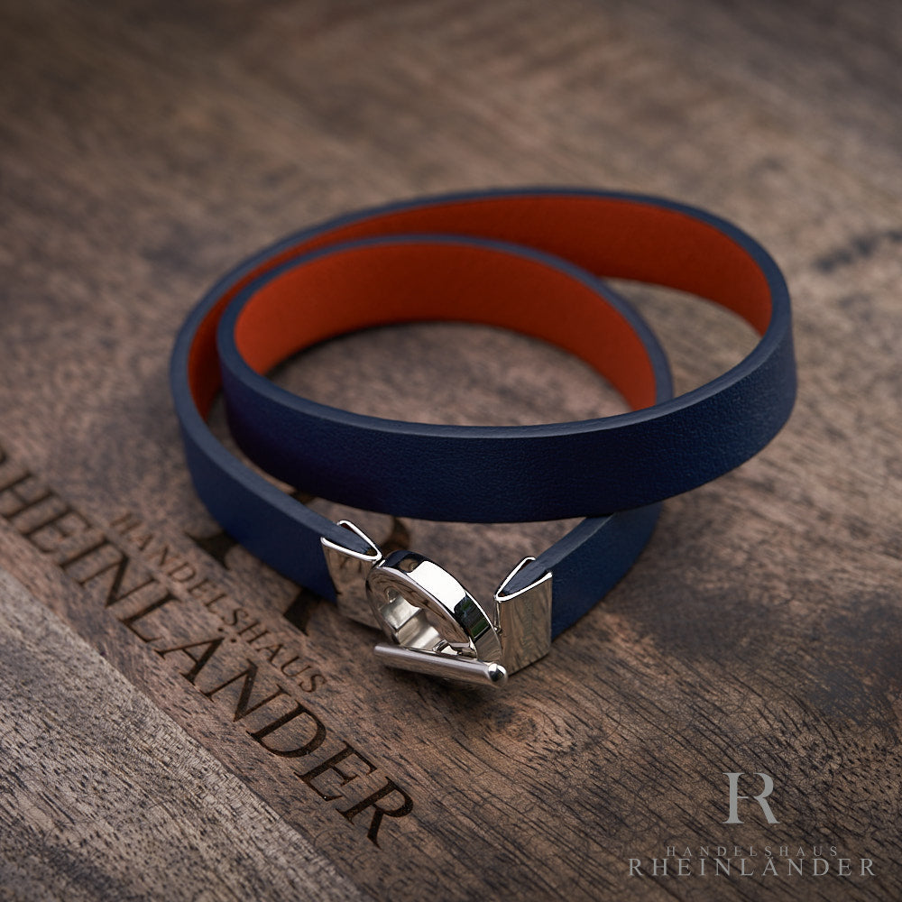 Blaues Armband, Innenseite orange, mit silbernem Knebelverschluss auf braunem Holz liegend fotografiert