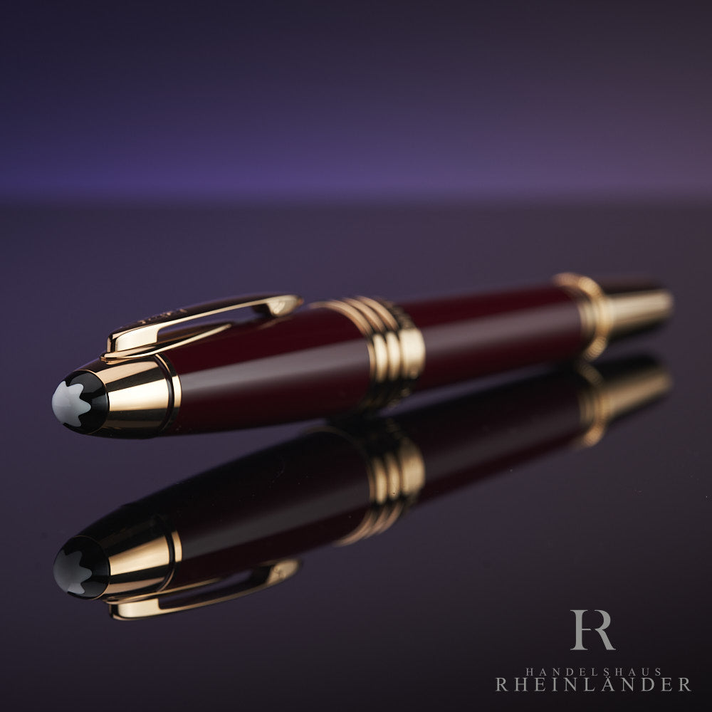 Dunkelroter Rollerball mit goldenen Beschlägen liegt auf spiegelndem Untergrund, die Kappe zeigt in Richtung Kamera