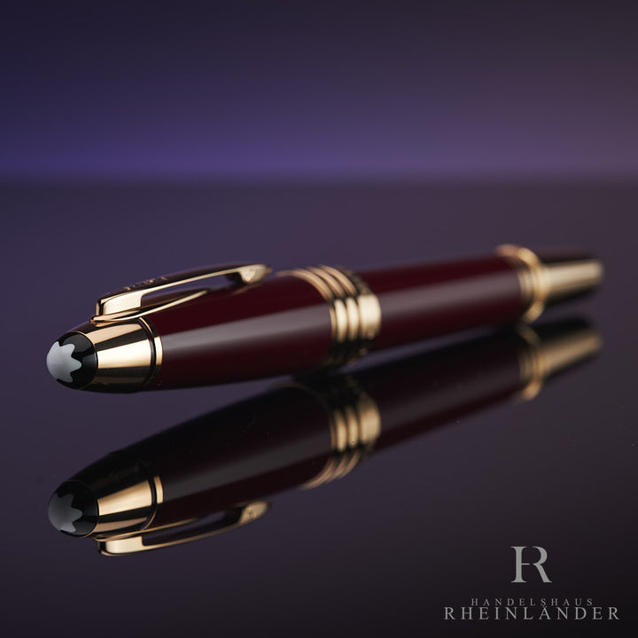 Dunkelroter Rollerball mit goldenen Beschlägen liegt auf spiegelndem Untergrund, die Kappe zeigt in Richtung Kamera