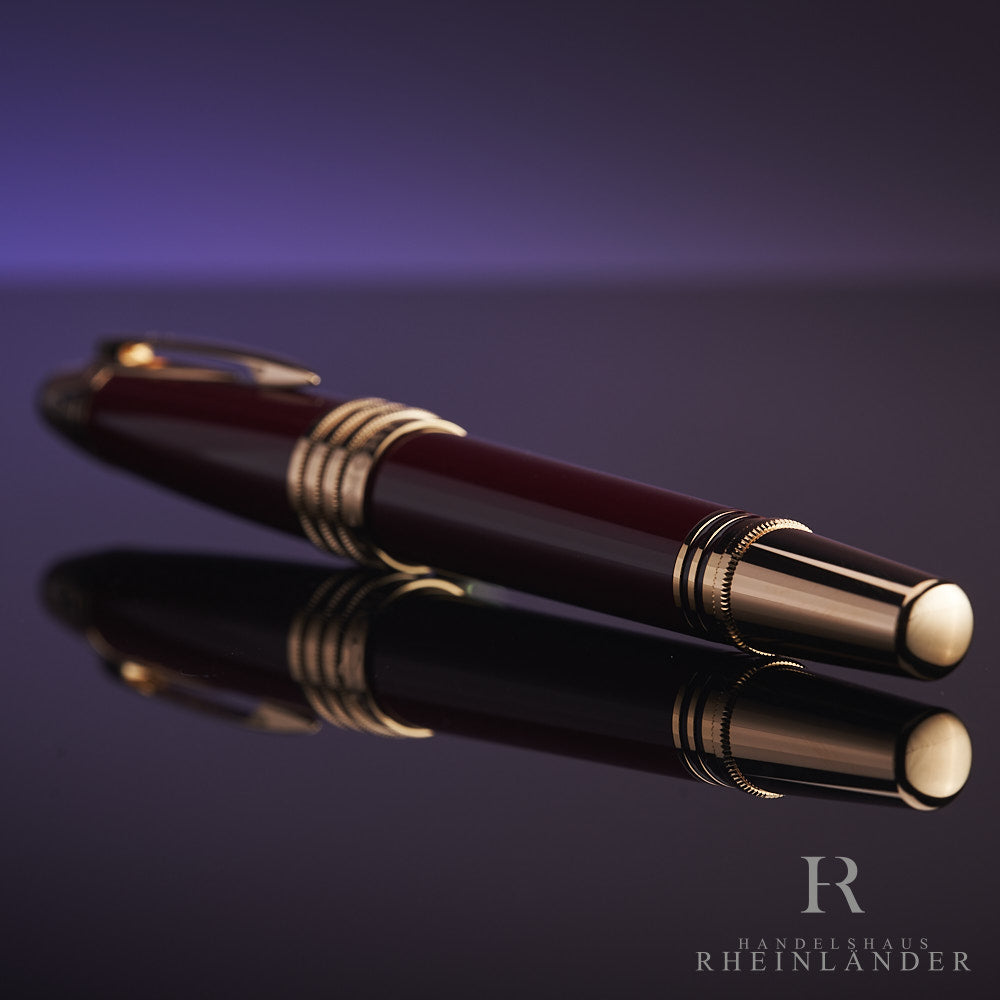 Dunkelroter Rollerball mit goldenen Beschlägen liegt auf spiegelndem Untergrund, der goldene Konus zeigt in Richtung Kamera