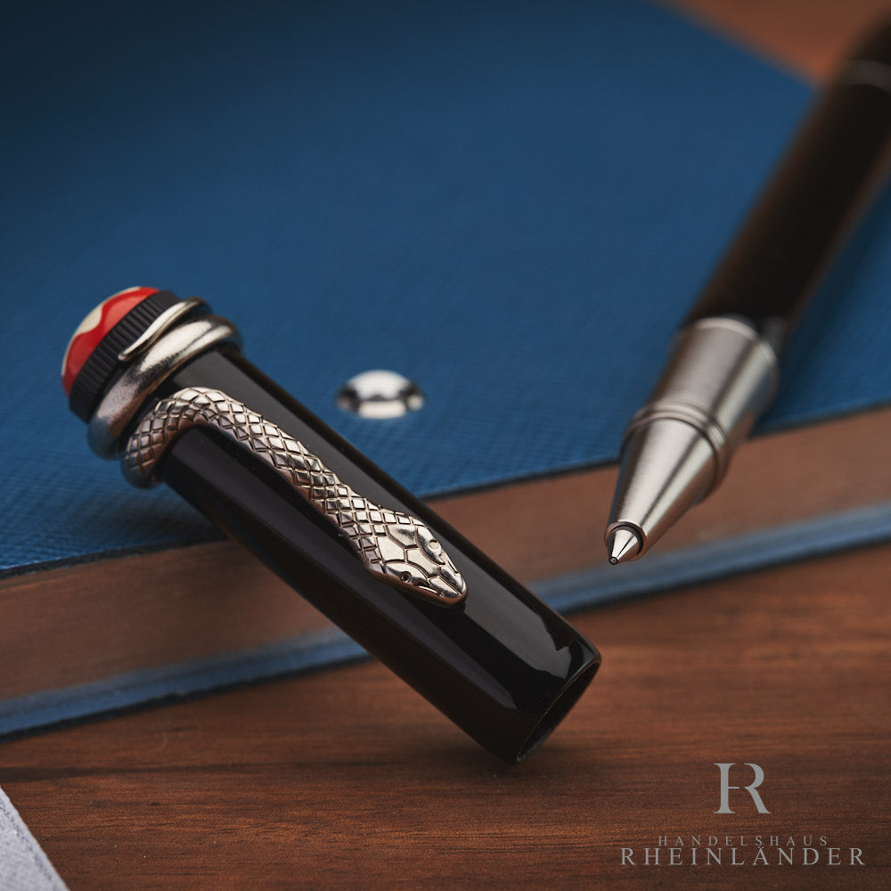 Schwarzer Rollerball liegt offen auf blauem Notizbuch, Kappe im Vordergrund an blauem Notizbuch lehnend