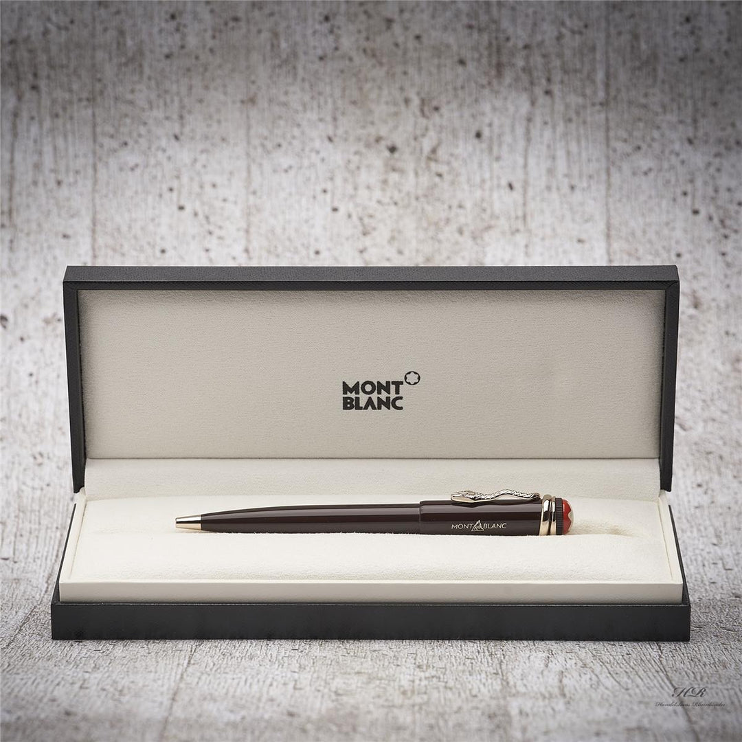 Brauner Kuli liegt in offener Originalbox vor grauem Hintergrund in Holzoptik