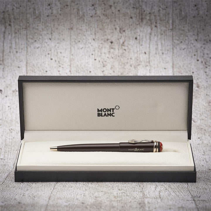Brauner Kuli liegt in offener Originalbox vor grauem Hintergrund in Holzoptik