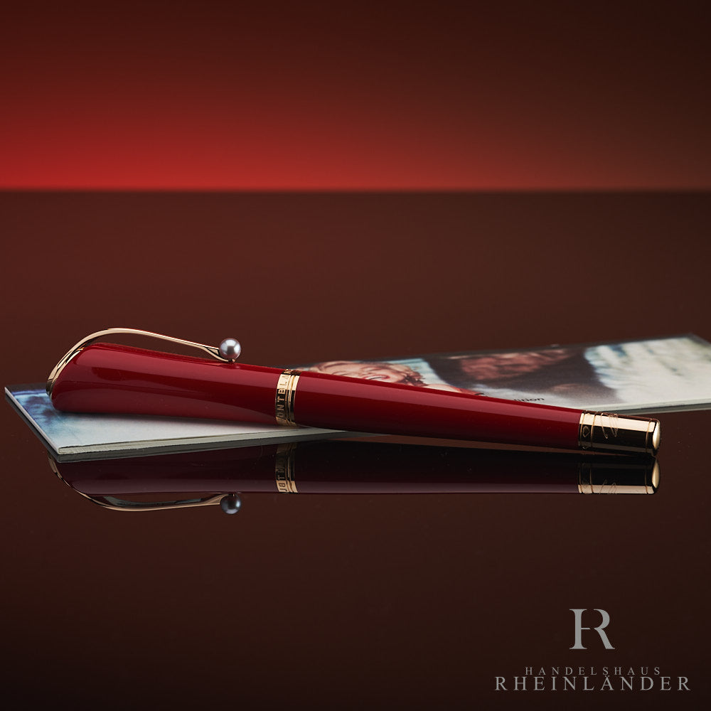 Roter Rollerball mit Goldbeschlägen und Zierperle am Clip liegt auf zugehörigem Serviceguide