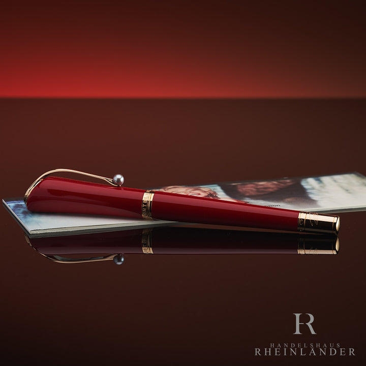 Roter Rollerball mit Goldbeschlägen und Zierperle am Clip liegt auf zugehörigem Serviceguide