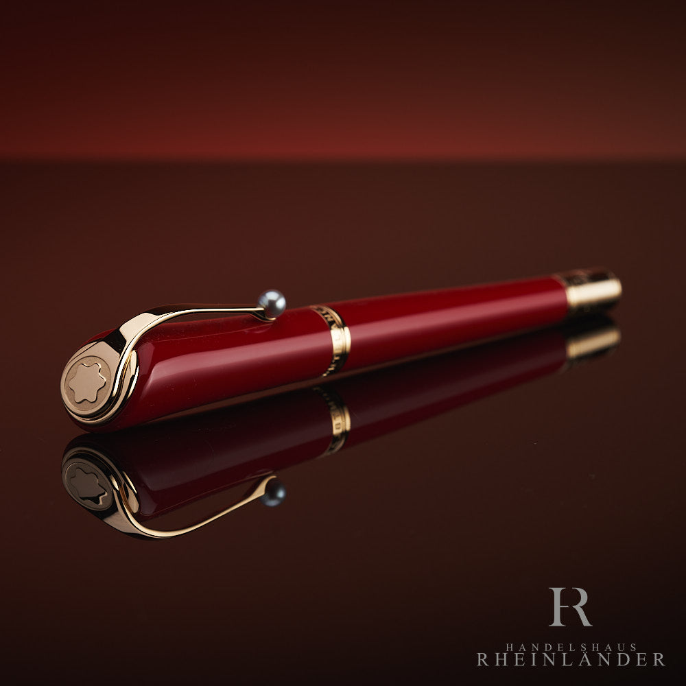 Roter Rollerball mit Goldbeschlägen und Zierperle am Clip liegt auf spiegelnder Oberfläche, Kappe voraus schräg zur Kamera gerichtet