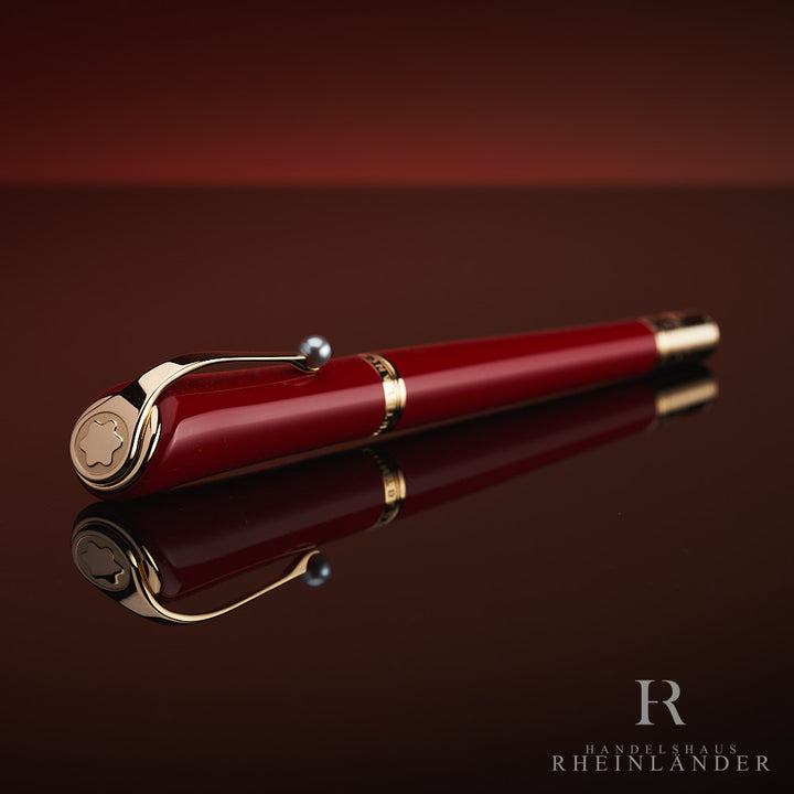 Roter Rollerball mit Goldbeschlägen und Zierperle am Clip liegt auf spiegelnder Oberfläche, Kappe voraus schräg zur Kamera gerichtet
