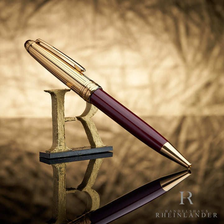 Dunkelroter Kugelschreiber mit goldener Kappe an 3D-Buchstabe R lehnend vor goldenem Knitteroptik-Hintergrund