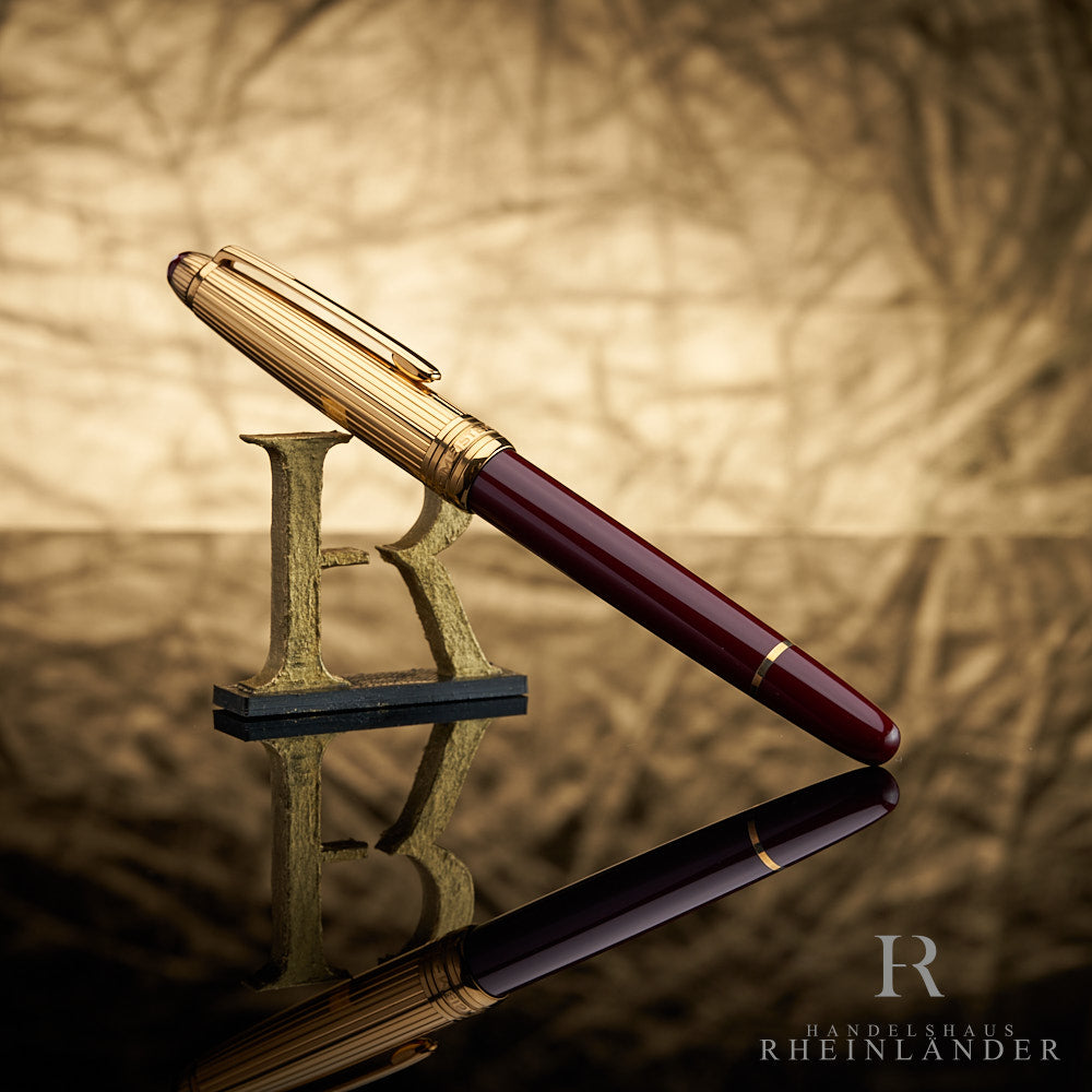 Dunkelroter Rollerball mit goldener Kappe an 3D-Buchstabe R lehnend vor goldenem Knitteroptik-Hintergrund