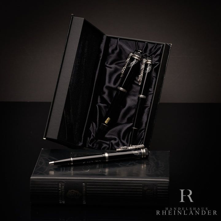 Set aus drei schwarzen Stiften, zwei davon in aufgestellter Originalbox, eins davor liegend auf Buchbox fotografiert
