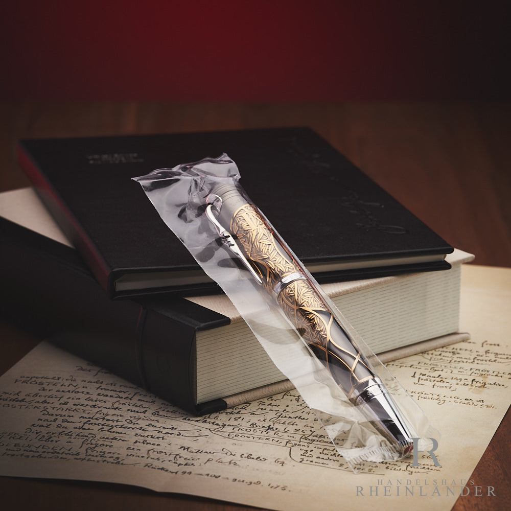 Rollerball in transparenter Schutzhülle lehnt an Editionsbox und Servicebuch. Darunter ein Schriftstück und Holzplatte.