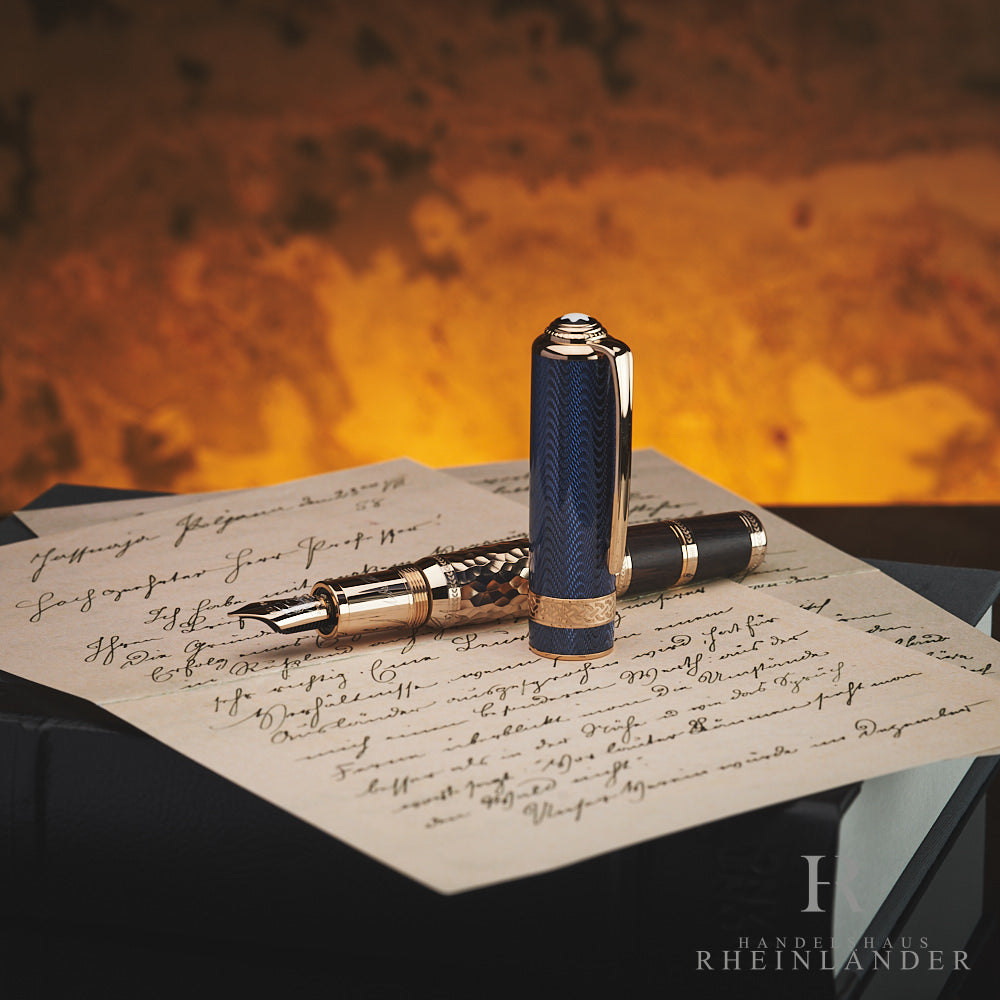 Blau-goldener Füller von Montblanc mit aufwendigen Details, mit geöffneter Kappe auf Schriftstück und Buch liegend fotografiert