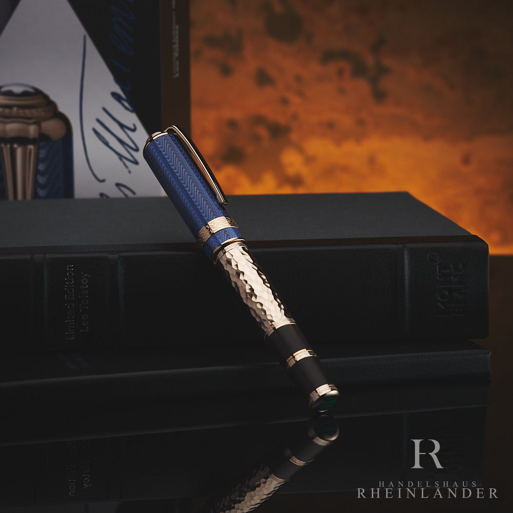 Füllfederhalter mit goldenem Korpus im Hammerschlag-Design und blauer Kappe mit Wellenmuster lehnt an Buchbox