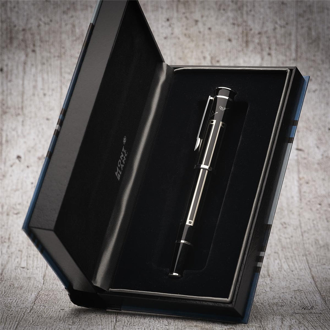 Silber-schwarzer Rollerball liegt in offener, halb aufgestellter Buchbox vor hellgrauem Holzoptik-Hintergrund