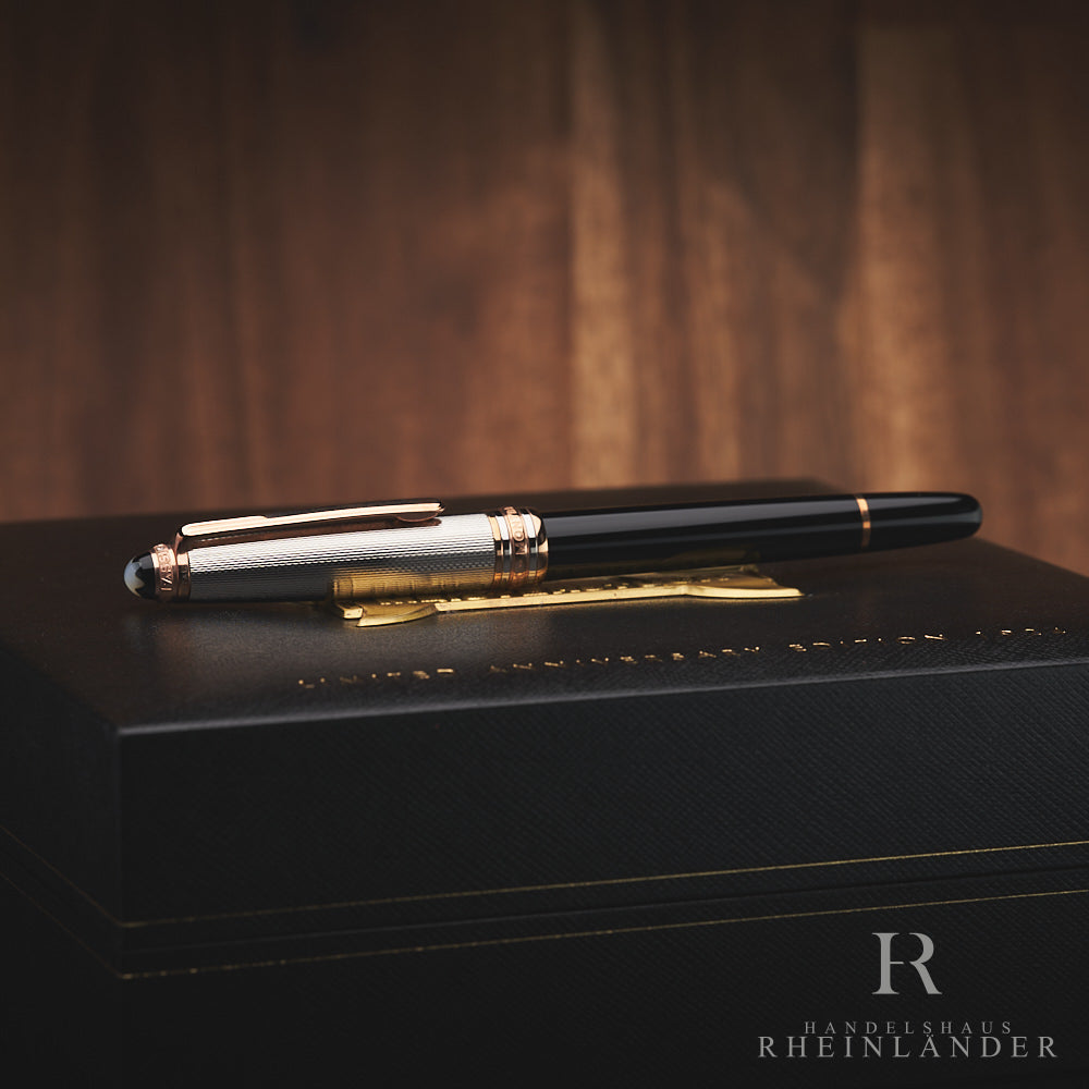 Schwarzer Rollerball mit silberner Kappe und rotgoldenen Beschlägen liegt auf schwarzer Originalverpackung