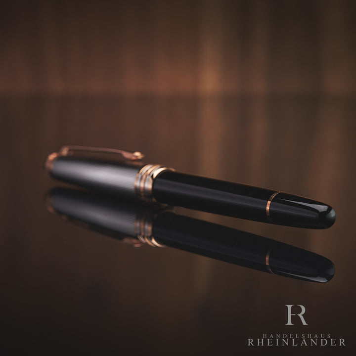Schwarzer Rollerball mit silberner Kappe liegt mit dem Korpus zur Kamera auf spiegelnder Oberfläche