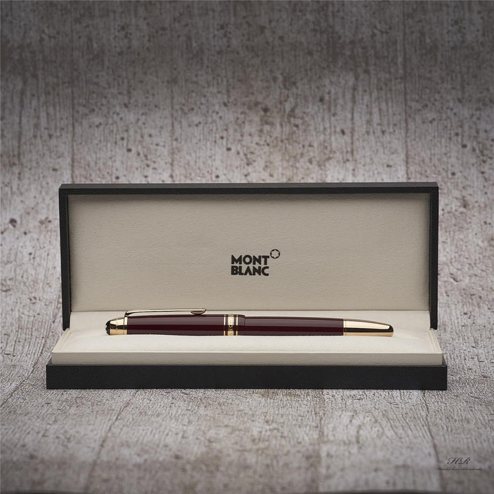 Burgunderfarbener Rollerball mit goldenen Beschlägen in offener Originalbox vor grauem Holzoptik-Hintergrund