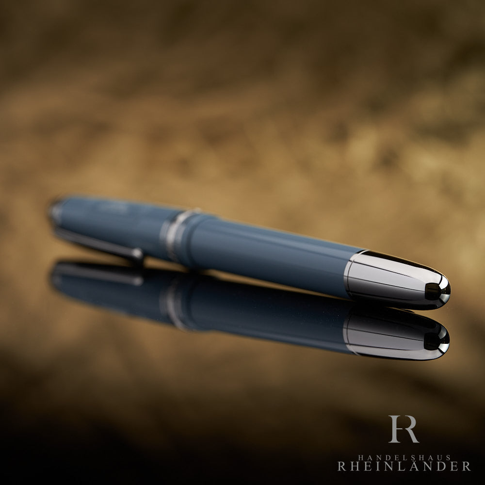 Graublauer Füller liegend auf spiegelnder Oberfläche fotografiert, der silberne Konus schräg zur Kamera gerichtet