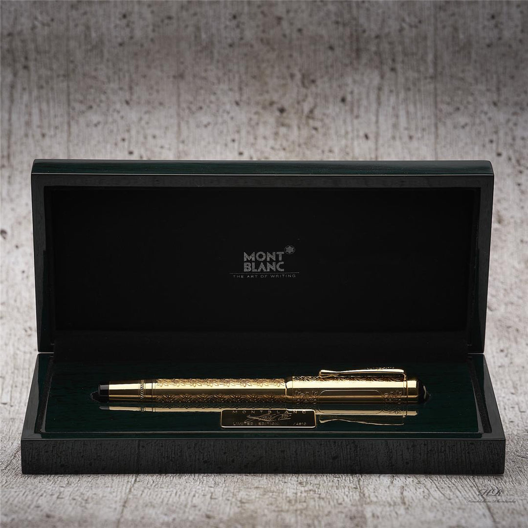 Goldener Füller von Montblanc mit kunstvollen Gravuren in geöffneter Geschenkschatulle liegend vor grauem Hintergrund in Holzoptik
