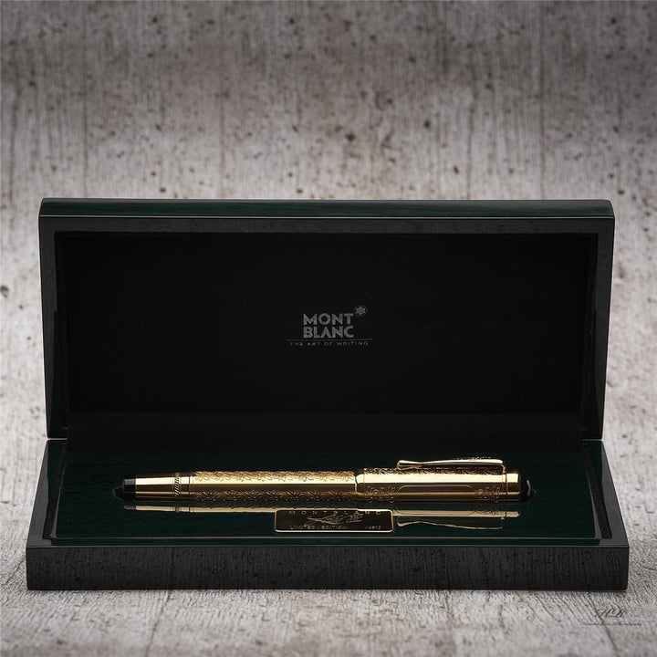 Goldener Füller von Montblanc mit kunstvollen Gravuren in geöffneter Geschenkschatulle liegend vor grauem Hintergrund in Holzoptik