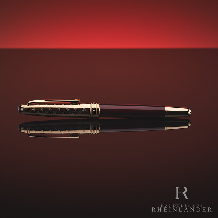 Burgundfarbener Rollerball mit goldener Kappe und Konus liegt horizontal auf spiegelnder Oberfläche vor rotem Hintergrund 