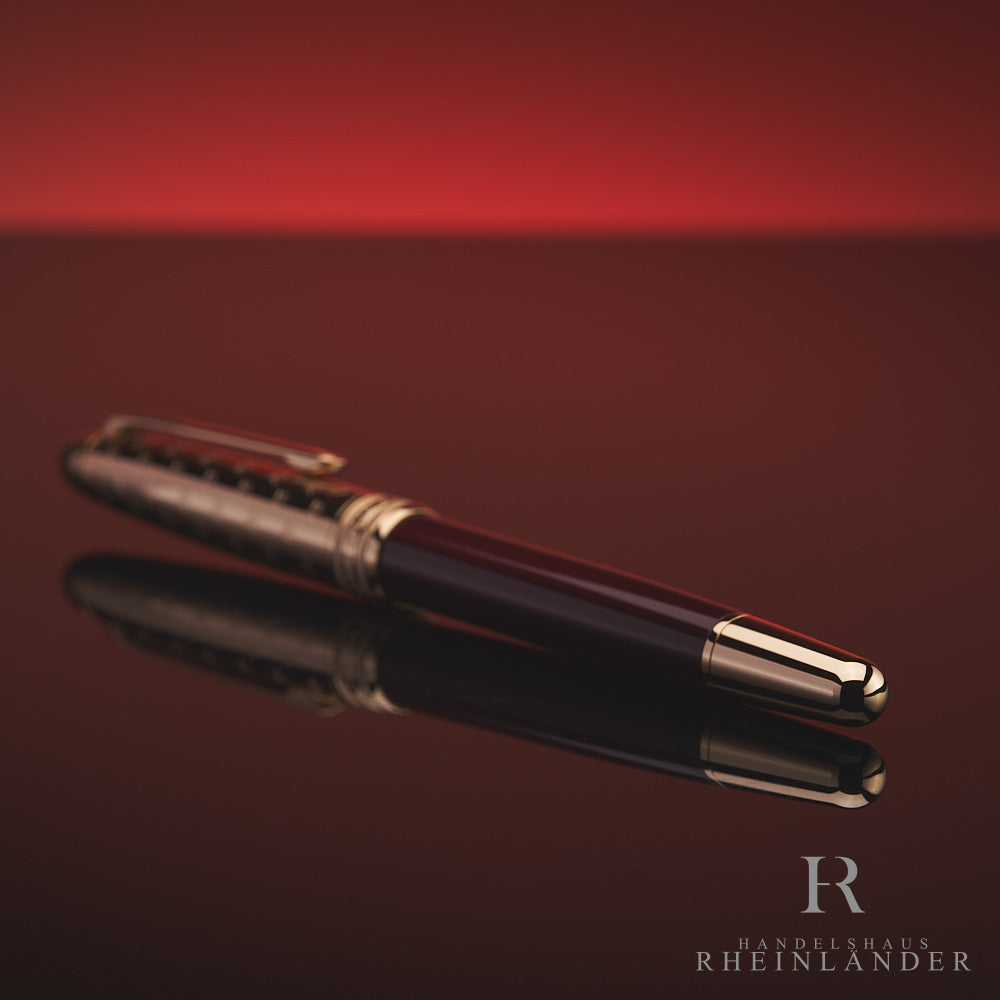 Burgundfarbener Rollerball mit goldener Kappe und Konus liegt mit dem Konus zur Kamera auf spiegelnder Oberfläche vor rotem Hintergrund 