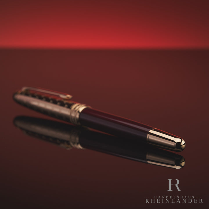 Burgundfarbener Rollerball mit goldener Kappe und Konus liegt mit dem Konus zur Kamera auf spiegelnder Oberfläche vor rotem Hintergrund 