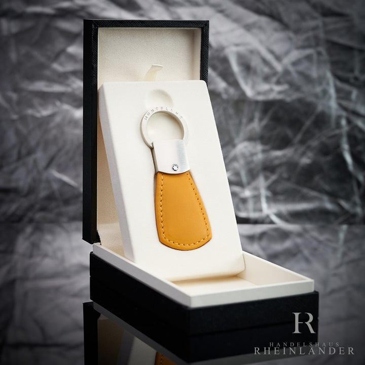 Gelber Montblanc Schlüsselanhänger in Originalverpackung offen stehend vor silbernem Hintergrund