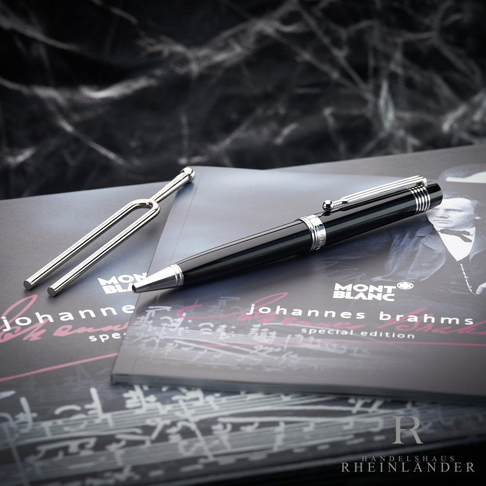 Schwarzer Kugelschreiber mit silberfarbenen Beschlägen liegt neben zugehöriger Stimmgabel auf dessen Originalverpackung