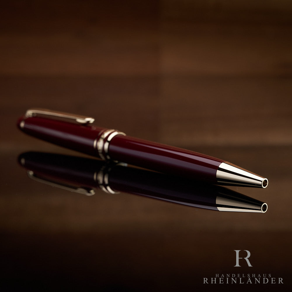 Bordeaux Kugelschreiber liegend mit der vergoldeten Spitze voran auf schwarzem Tisch