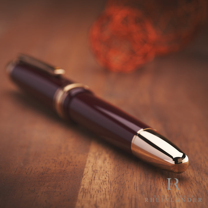 goldener Konus des Montblanc LeGrand Petit Prince Füllfederhalters liegend auf Holztisch mit bordeaux-rotem Schaft