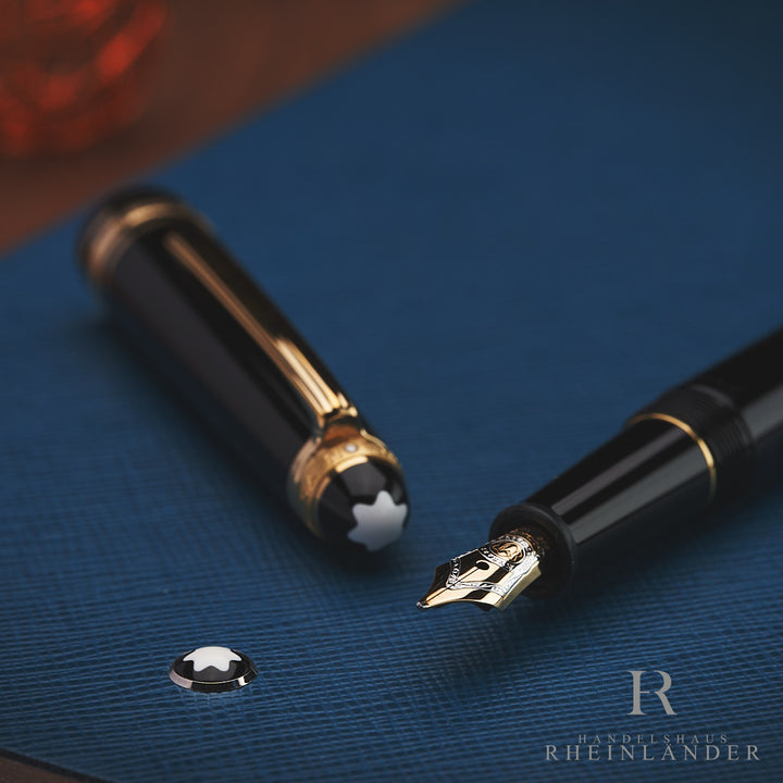 offener Montblanc Füller mit Goldfeder und Kappe liegend auf blauem Leder Notizbuch mit Montblanc Emblem