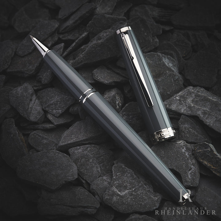 Grauer PIX Rollerball von Montblanc, daneben graue Kappe mit silbernen Beschlägen, auf dunkelgrauem Steinboden fotografiert