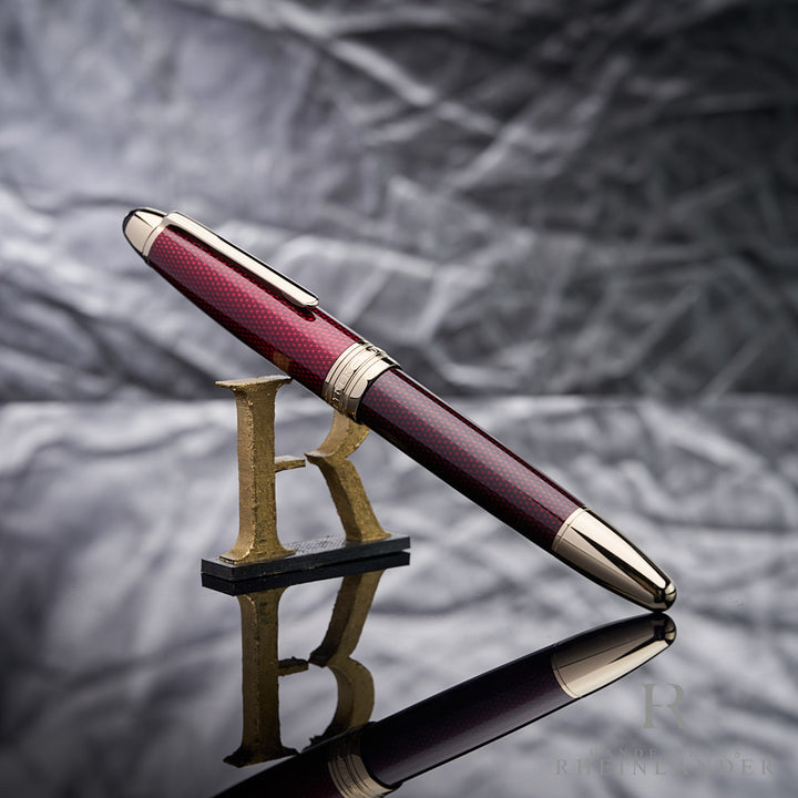 Montblanc Solitaire Golden Hour Rollerball angelehnt an das Handelshaus Rheinländer Logo vor silbernem Hintergrund